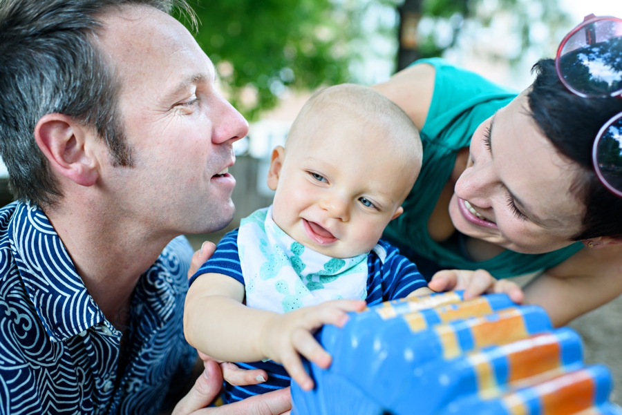 A baby rides a horse at the park with mom and dad.